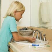 A girl washing her hands in a sink with travel-size toothpaste next to her