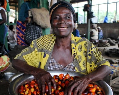 A woman posing with a bucket of oil palm fruit