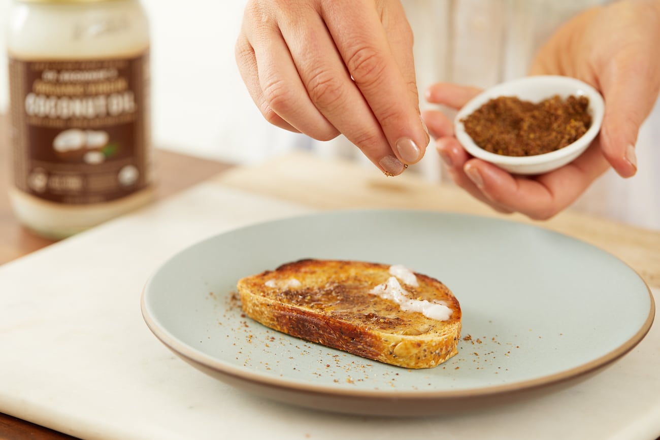 Sprinkling cinnamon and sugar mixture on toast with melted coconut oil