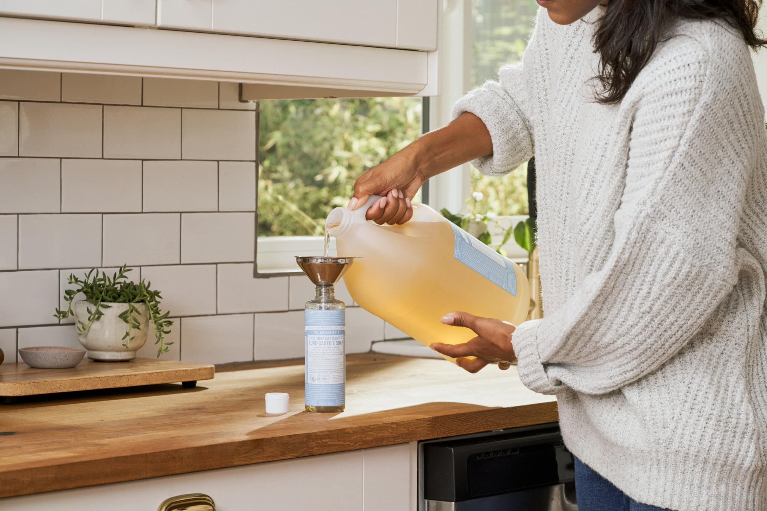 person refilling Dr. Bronner's soap bottle from bulk bottle